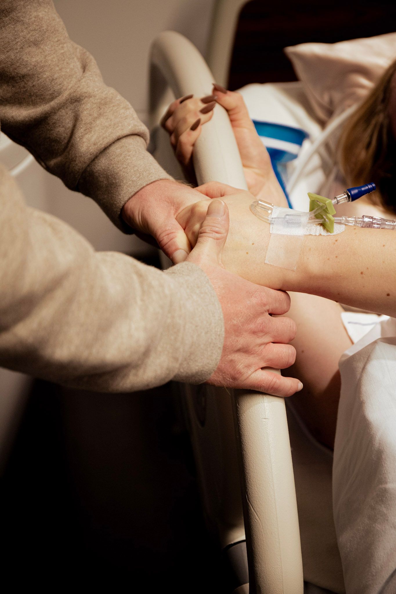 A comforting hand holds and supports someone pushing during a birth in a hospital bed with IV lines attached.
