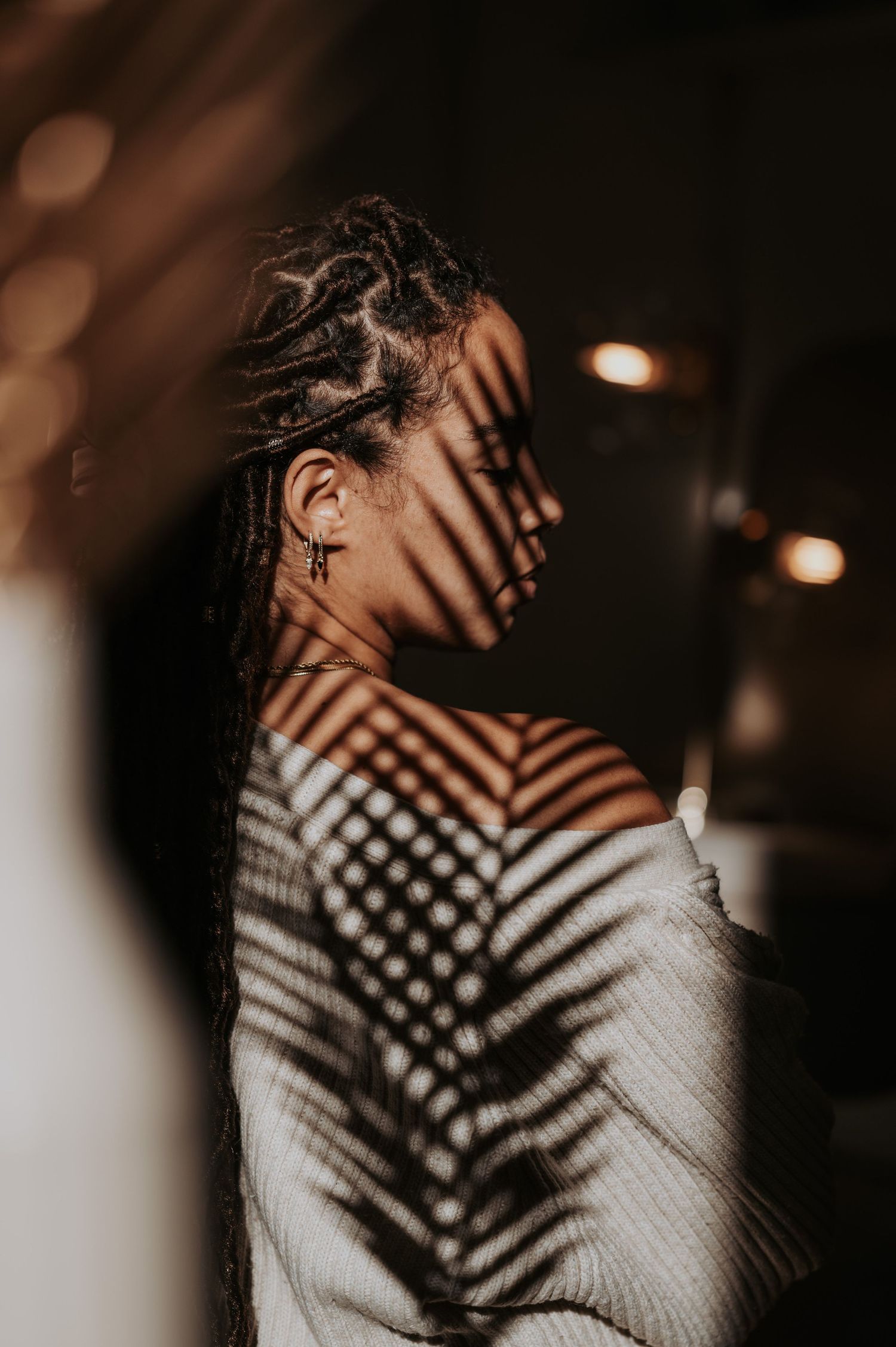Artistic portrait with palm leaf shadow patterns creating dramatic lighting effects in a moody dark setting.