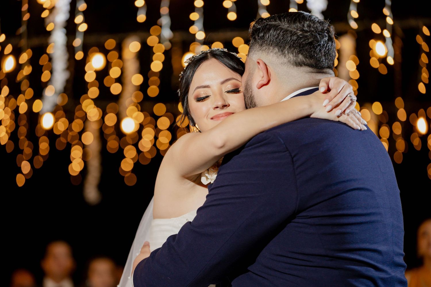 Intimate dance moment under romantic hanging lights at wedding reception.