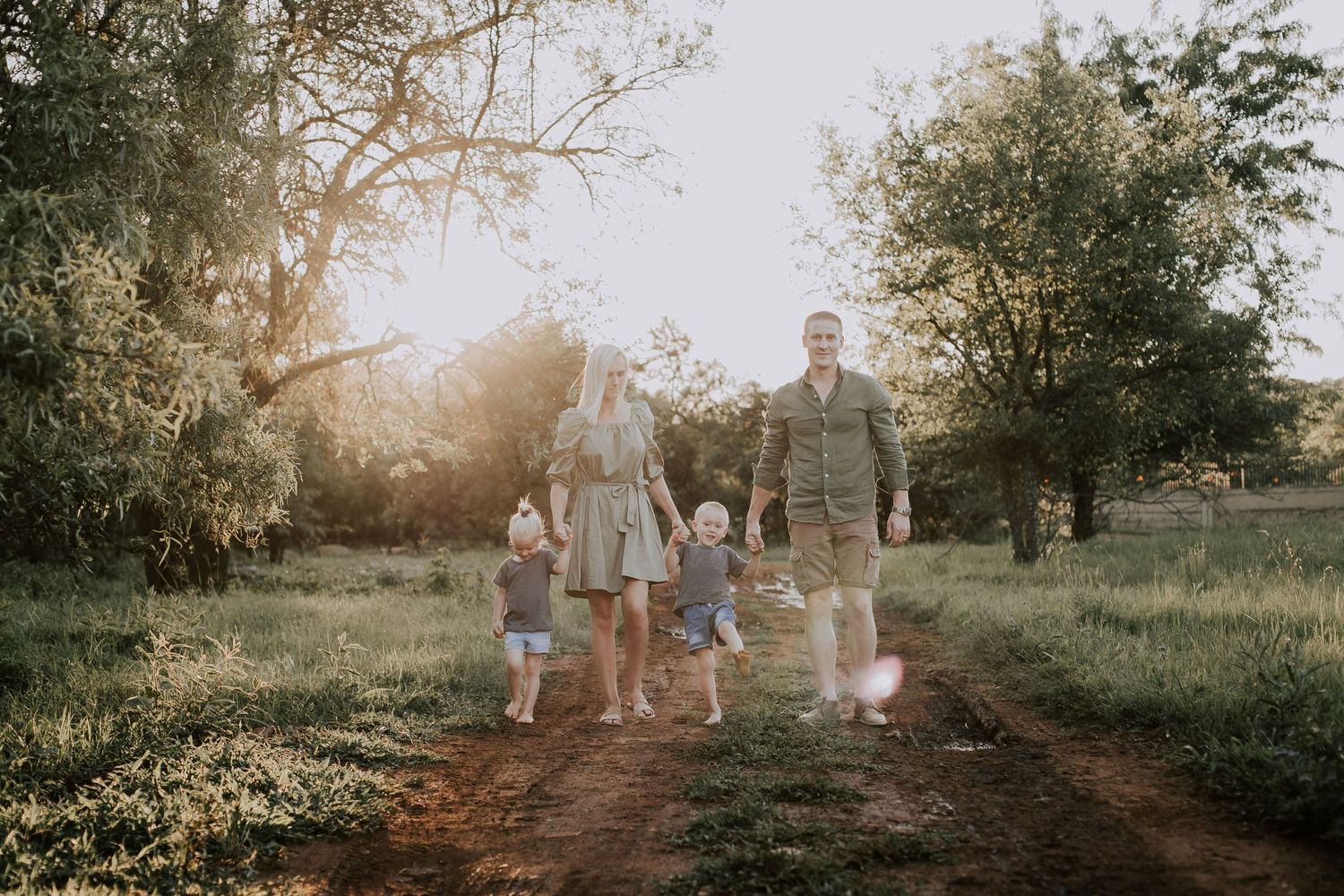 A family walking together on a dirt path during golden hour with sunflare through the trees.