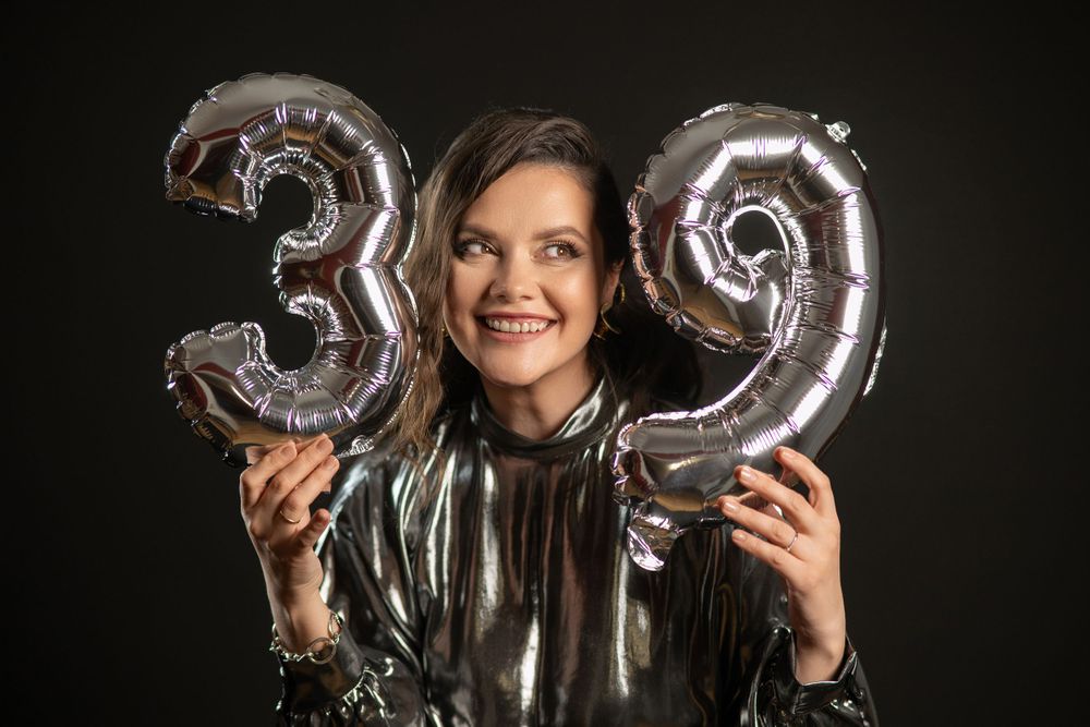 Silver metallic balloon numbers 39 held against dark background by someone in a shiny jacket.