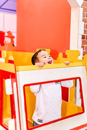 Excited young boy playing inside a colorful red and yellow play structure at an indoor children's museum.