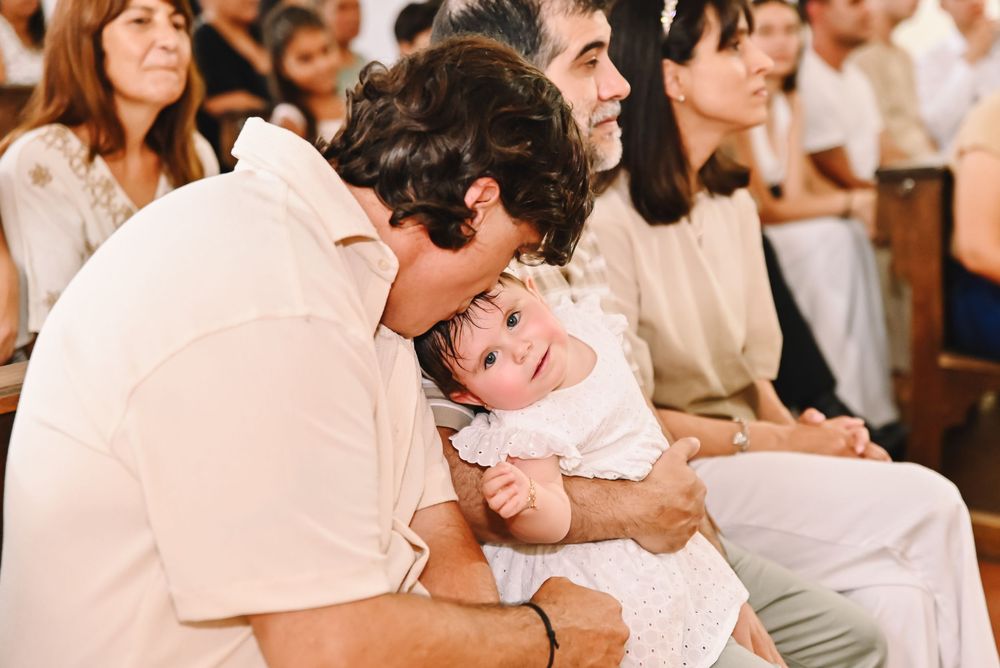 Man kissing baby at a church ceremony, with guests seated in pews in the background.