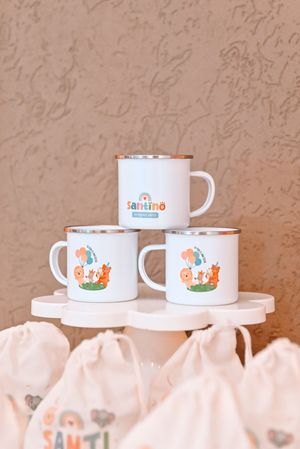 Three white enamel mugs with Santino design stacked on a display stand with gift bags below.