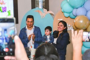 Family celebrating baby’s first birthday party with teal and gold balloon decorations at a festive indoor event.