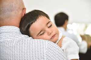 A sleeping child rests peacefully on someone's shoulder wearing a white shirt.