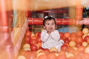Baby sitting in orange ball pit making excited expression during playtime.