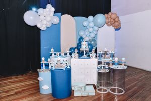 First birthday party decoration setup with blue and white balloon arch and dessert displays.