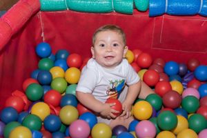 Infant enjoying playtime in a red ball pit filled with colorful plastic spheres.