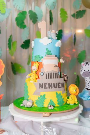 Jungle themed first birthday cake with safari animals and green leaves on a white cake stand.