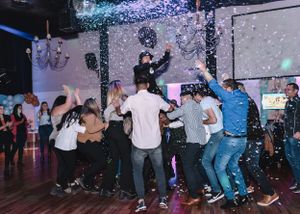 Crowd dancing and celebrating under falling confetti at an indoor party.