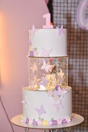 Elegant two-tier white birthday cake decorated with delicate purple and yellow butterflies and number one topper.