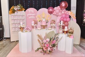 Pink and white party decorations with balloons and floral arrangements on display pedestals.