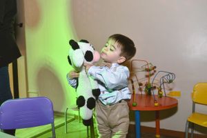 Child playing with large plush panda toy against light green wall.
