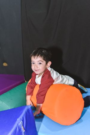 Playful scene on colorful gym mats with bright orange cushion.
