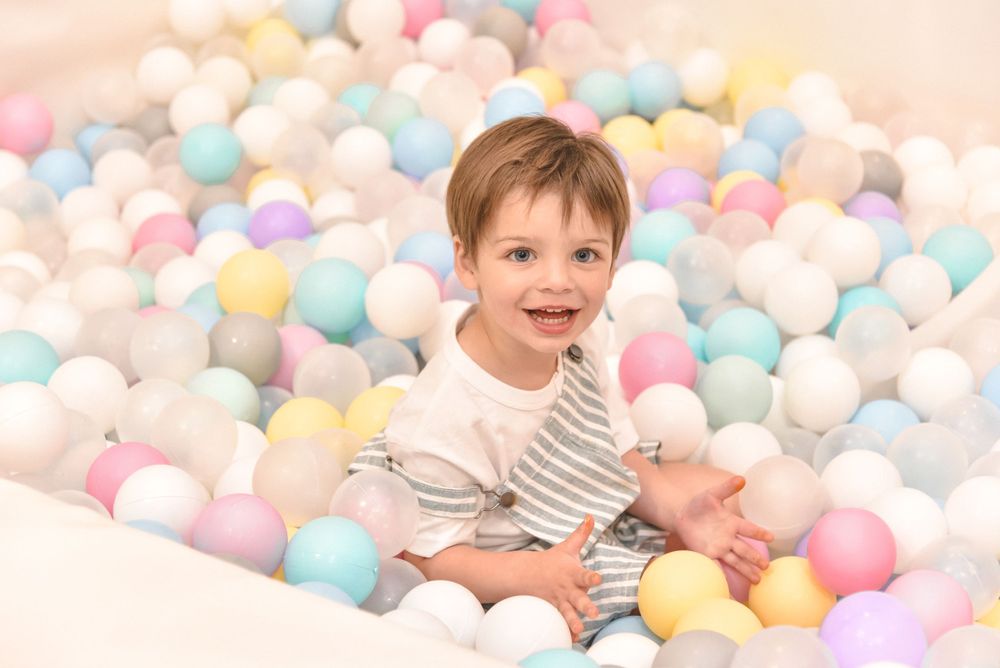 Child playing in a ball pit filled with pastel colored balls.