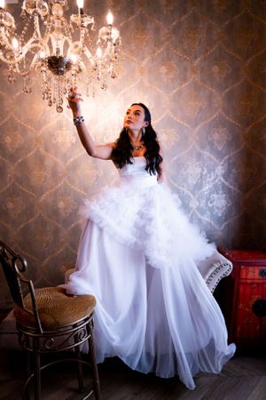 Dreamy bridal portrait reaching toward crystal chandelier in romantic setting, during a bridal portrait session.