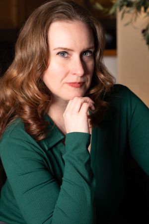 Portrait of woman in green sweater with styled curls in warm indoor lighting, captured in a studio photography session.