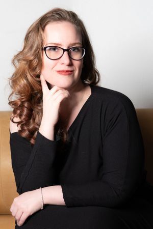 Professional headshot of woman in black sweater and glasses with styled hair, captured in a studio photography session.