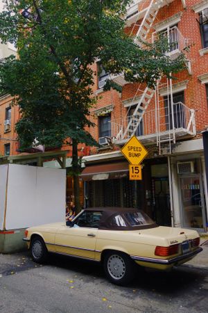 A classic Mercedes convertible parked on a city street with brick buildings and fire escapes in New York.