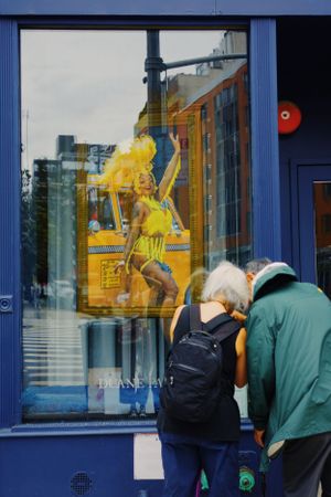 Two people looking at a storefront window display featuring a vibrant yellow athletic mannequin in a dynamic pose.