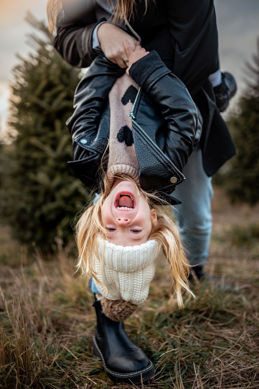 A playful upside-down moment captured at a Christmas tree farm with winter attire and pure joy.