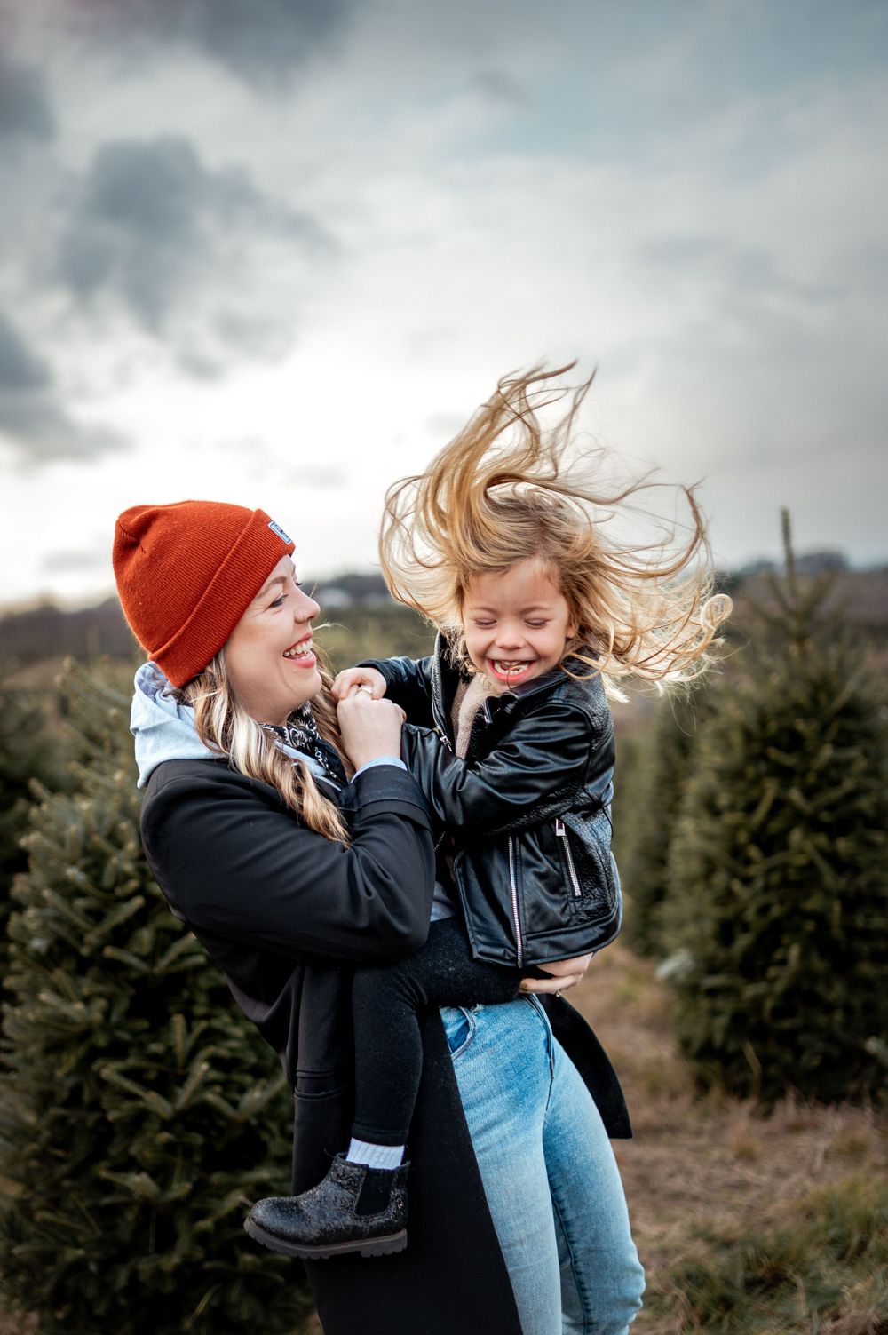 A joyful moment captured at a Christmas tree farm with wind blowing through hair on an overcast day.