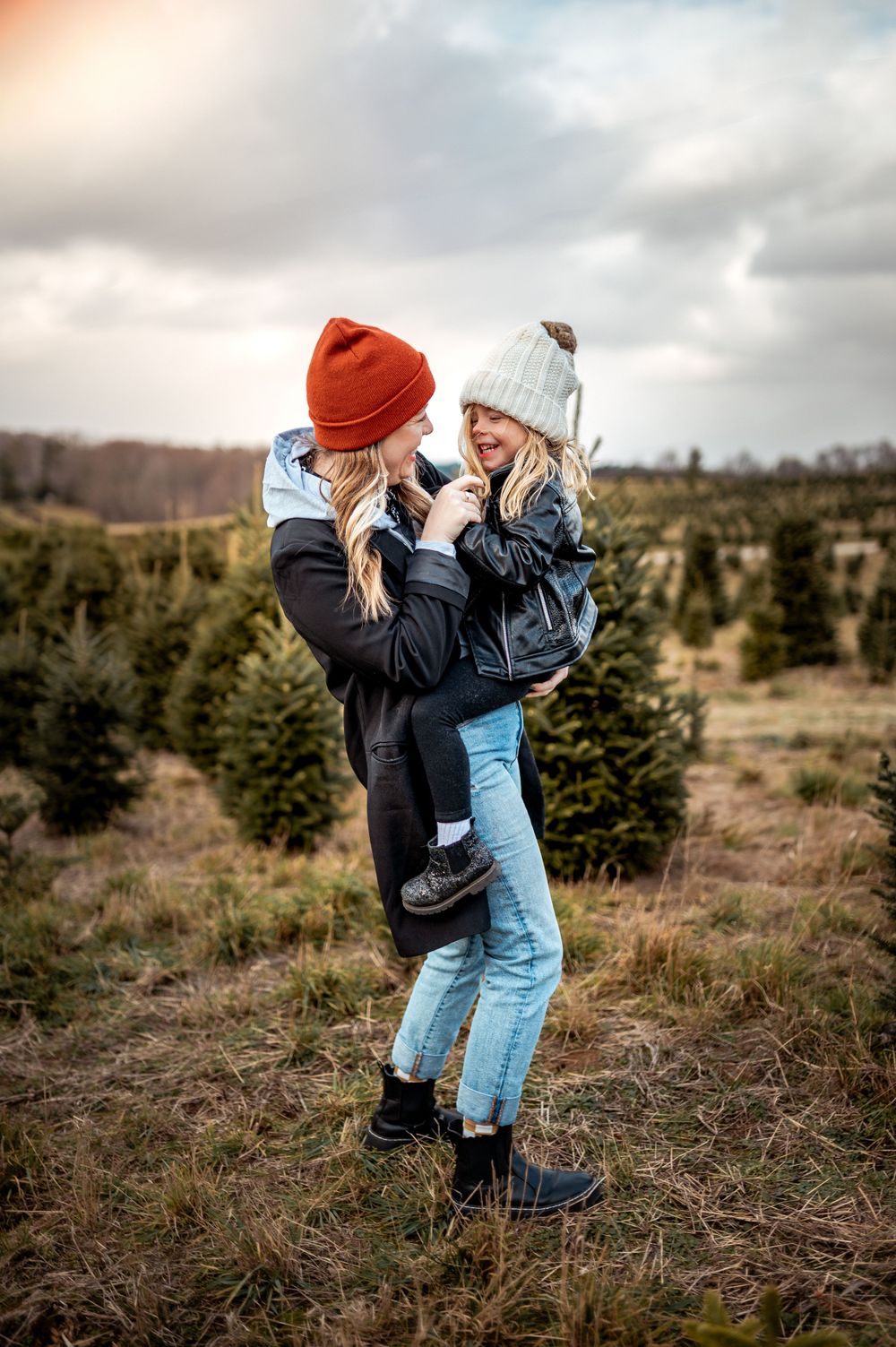 Two friends sharing a joyful moment while wearing winter beanies at a Christmas tree farm in the countryside.