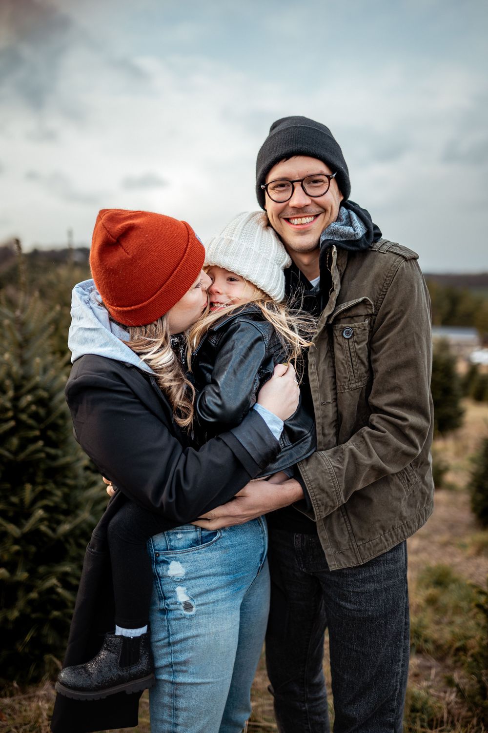 A couple and their bundled baby enjoying a winter day together at a Christmas tree farm.