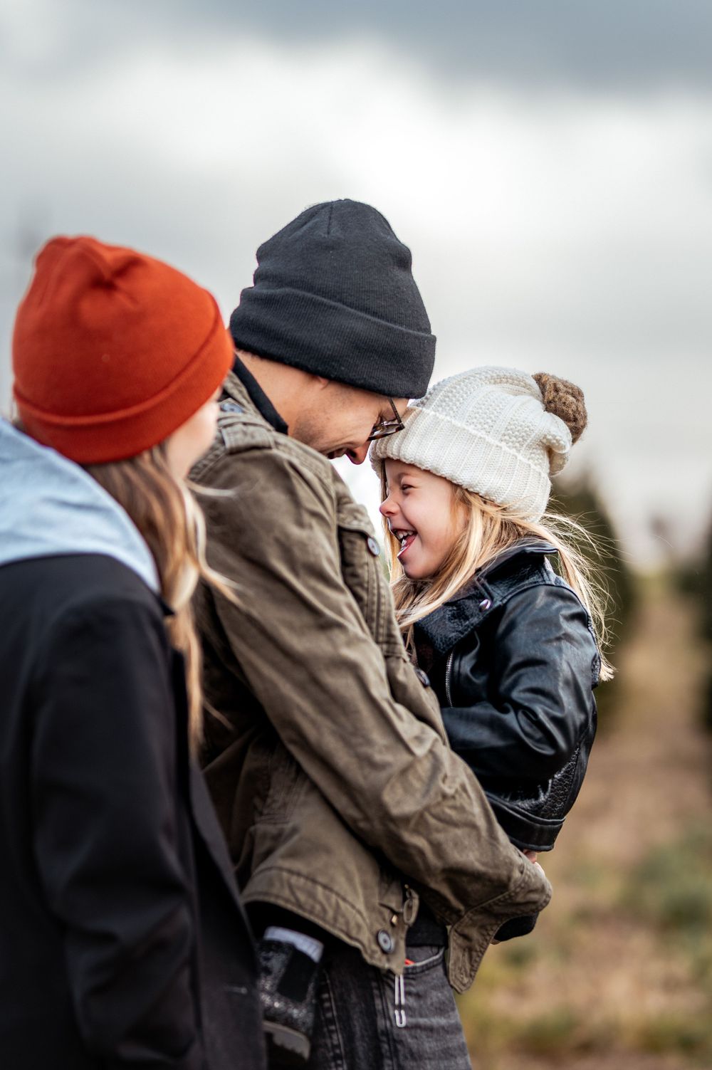A candid moment of laughter shared between three people at a tree farm on a cloudy winter afternoon.