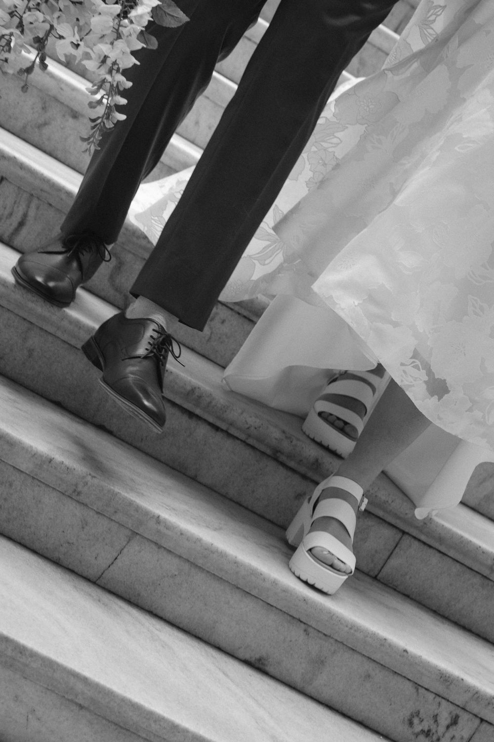 Black and white close-up of bride and groom shoes on marble steps at wedding venue.