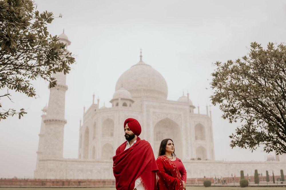 A beautiful foggy morning at the iconic Taj Mahal in Agra, with two figures in red attire in the foreground.