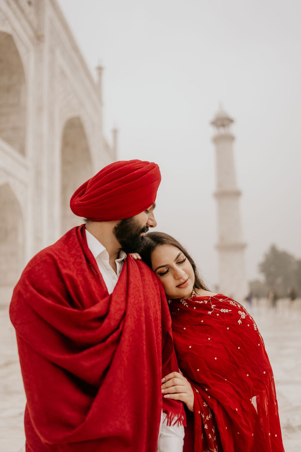 A couple in red traditional attire embrace near the Taj Mahal in India during a romantic photo session.