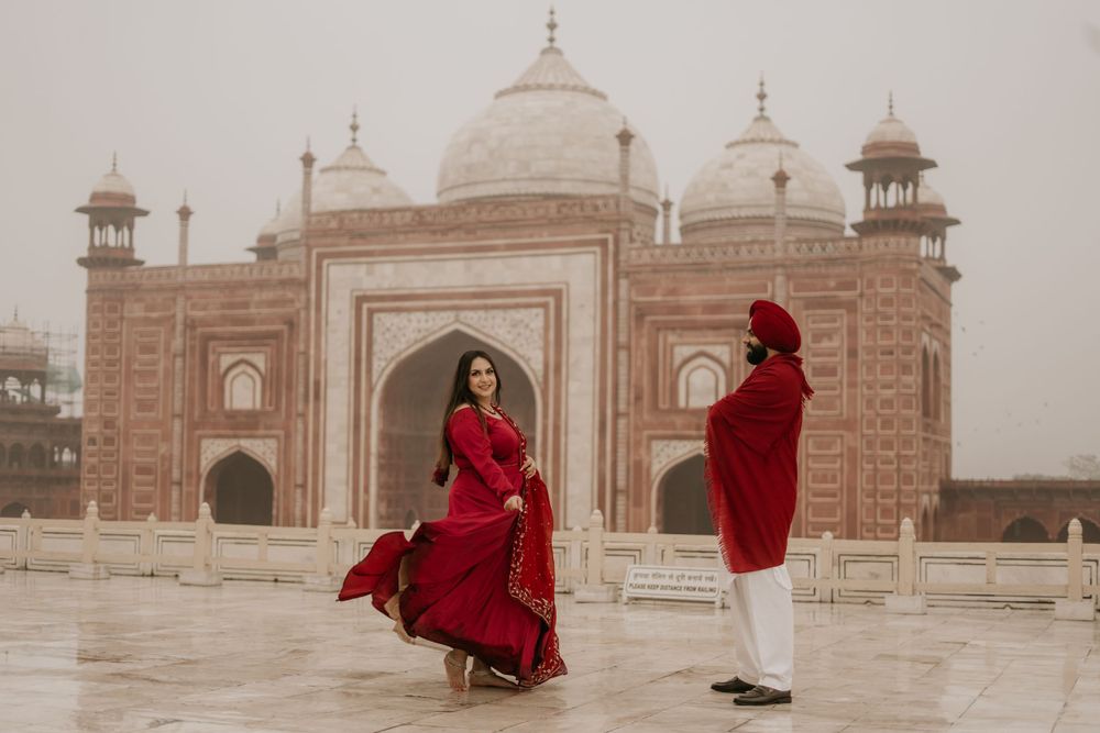 Two people in red attire posing in front of an ornate mosque building with domed architecture.