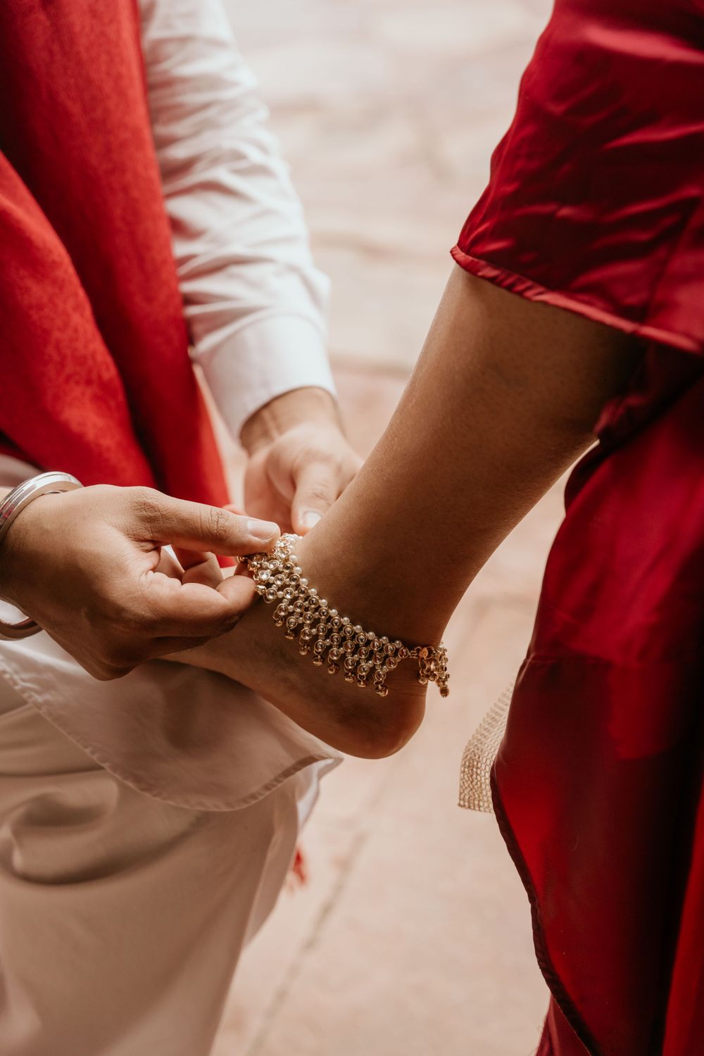 Close-up of hands fastening an ornate gold anklet against red and white fabric.