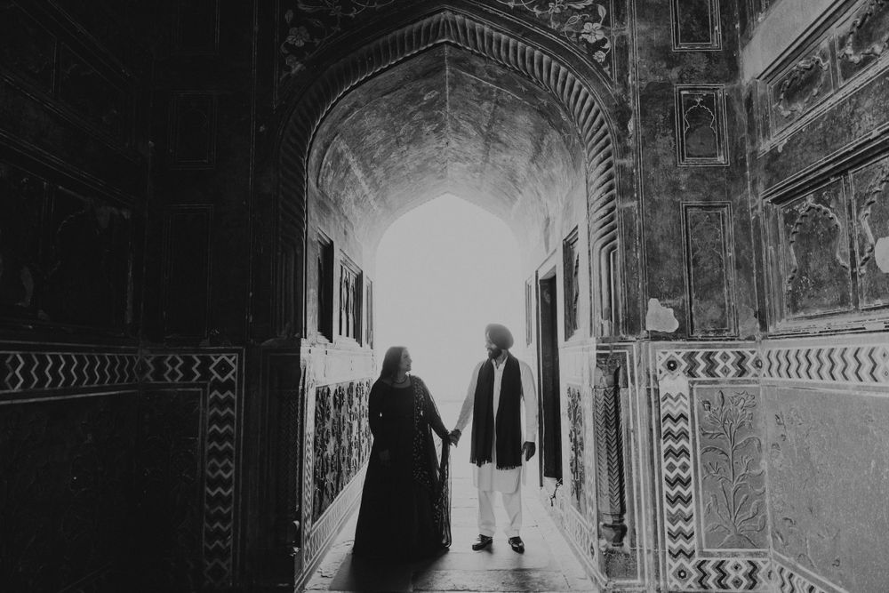 Two figures in silhouette walk through an ornate archway corridor with intricate patterns and architectural details.