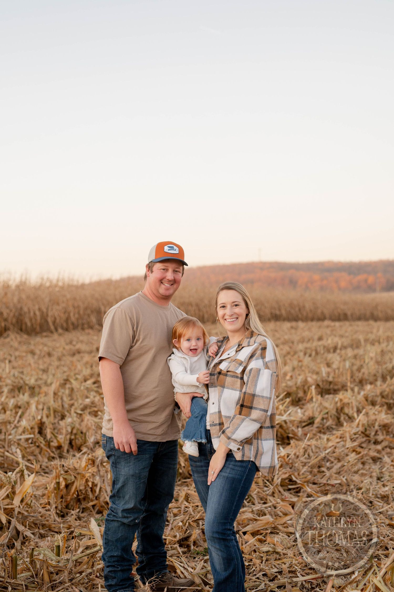 Family photo in autumn cornfield with rolling hills in background.