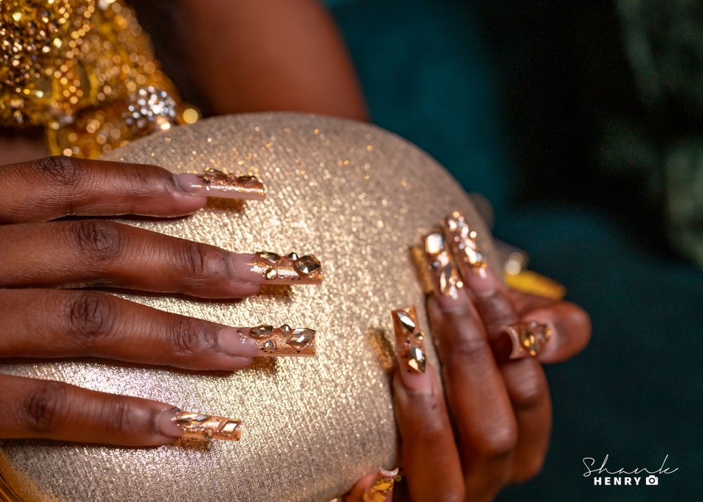 Beautifully decorated hands with intricate henna designs hold a shimmering gold purse against a teal background.