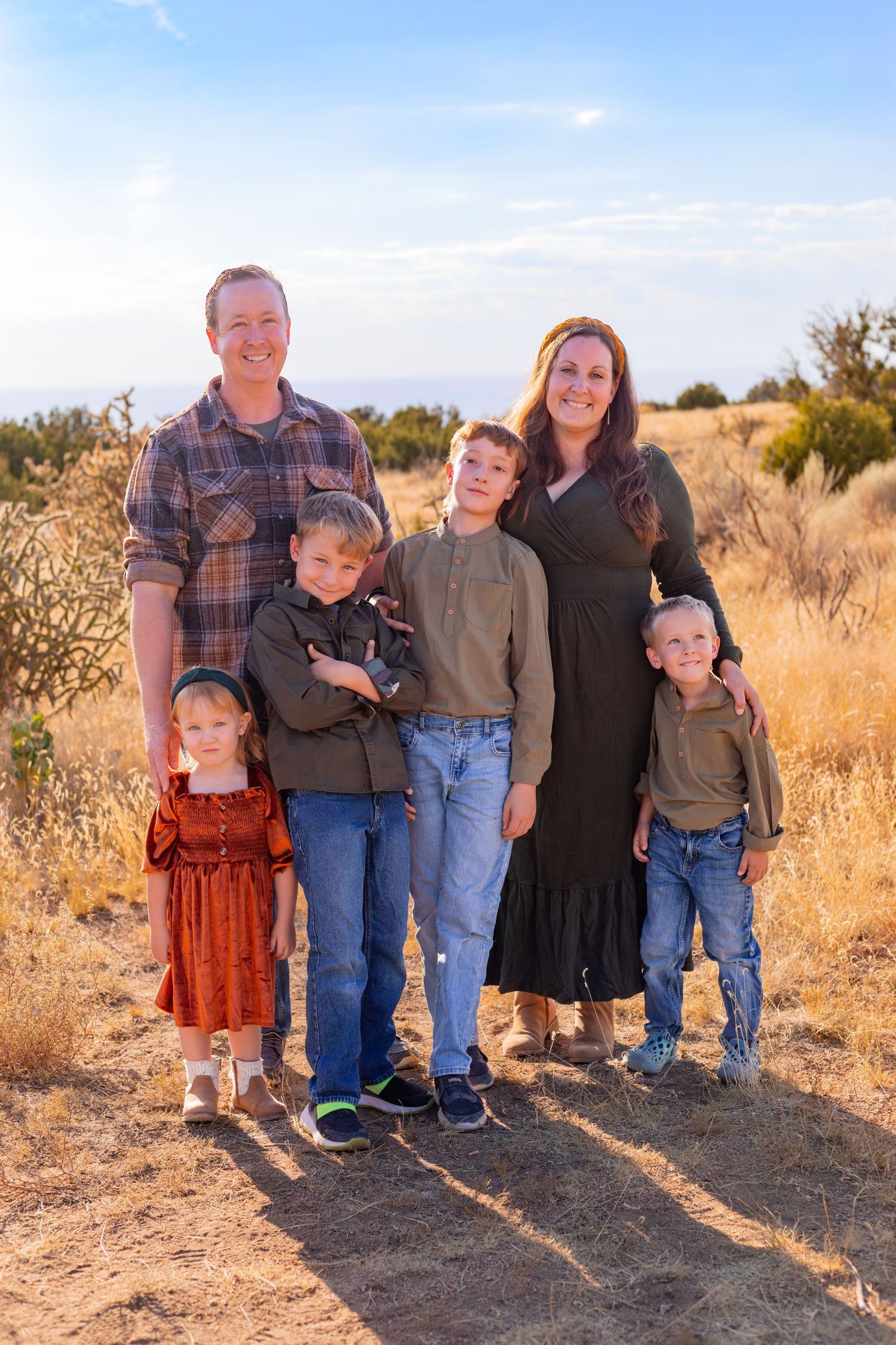 Family of six poses together on desert trail during outdoor portrait session.