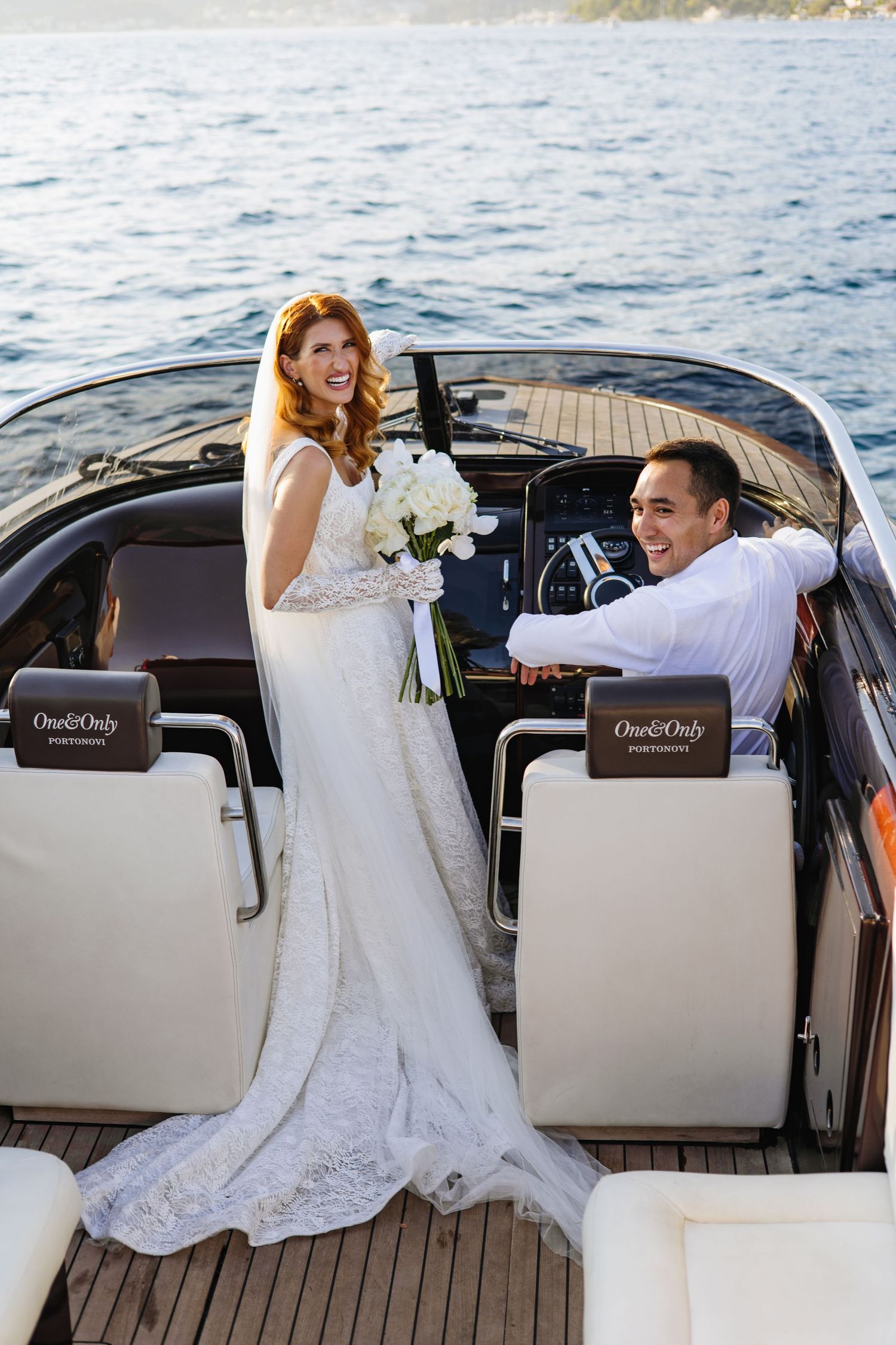 A wedding couple enjoys a luxurious boat ride on the water with white leather seats and teak decking.