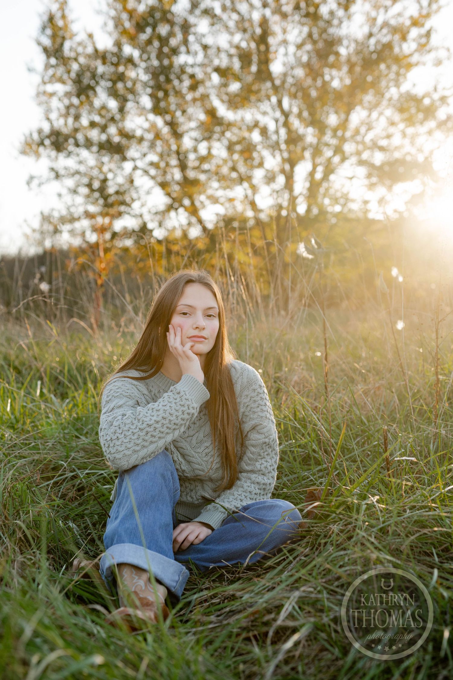 Natural outdoor portrait with someone sitting in golden sunlit grass wearing a chunky knit sweater.