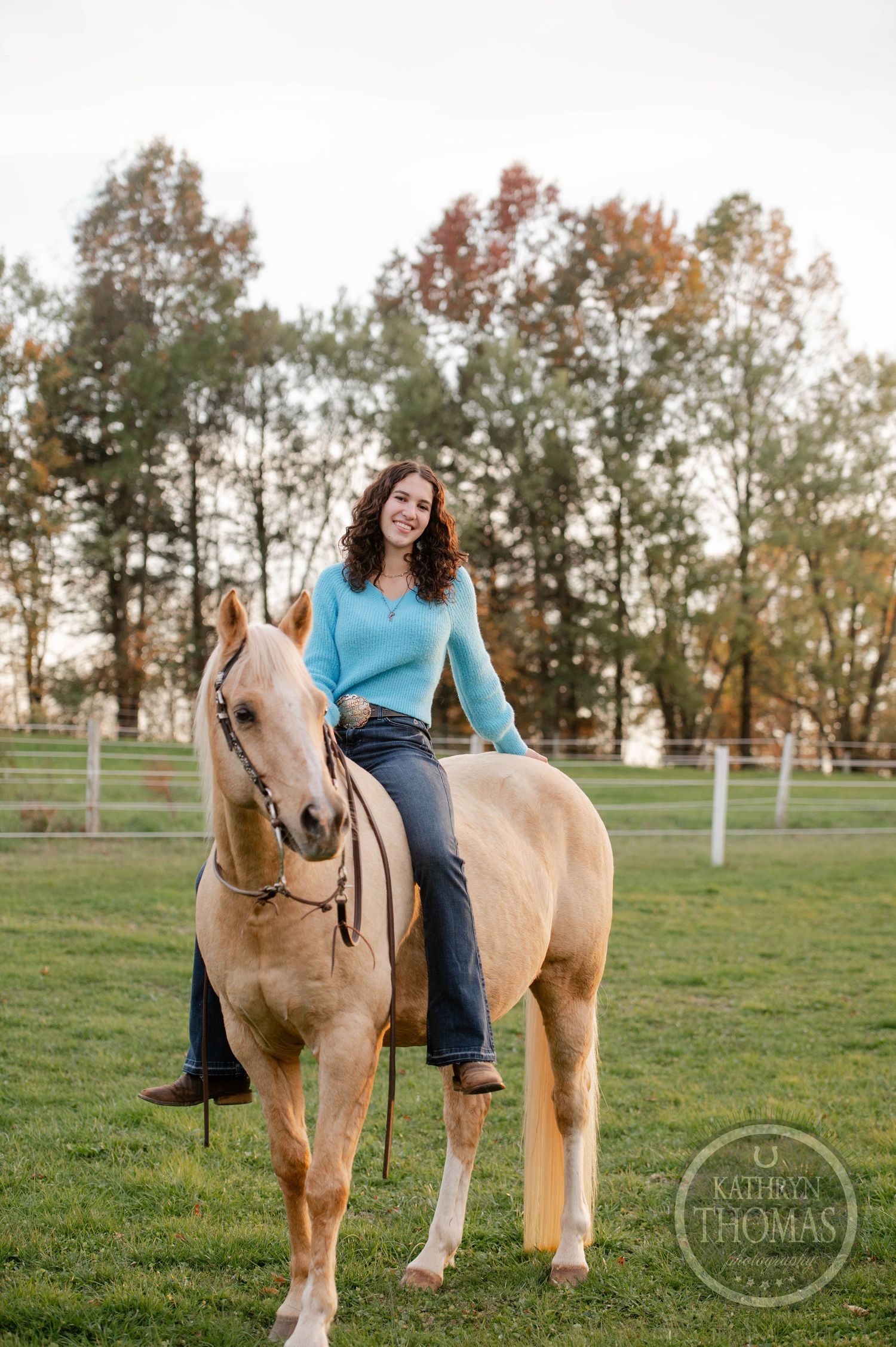 Casual portrait of rider atop palomino horse in outdoor arena during autumn.