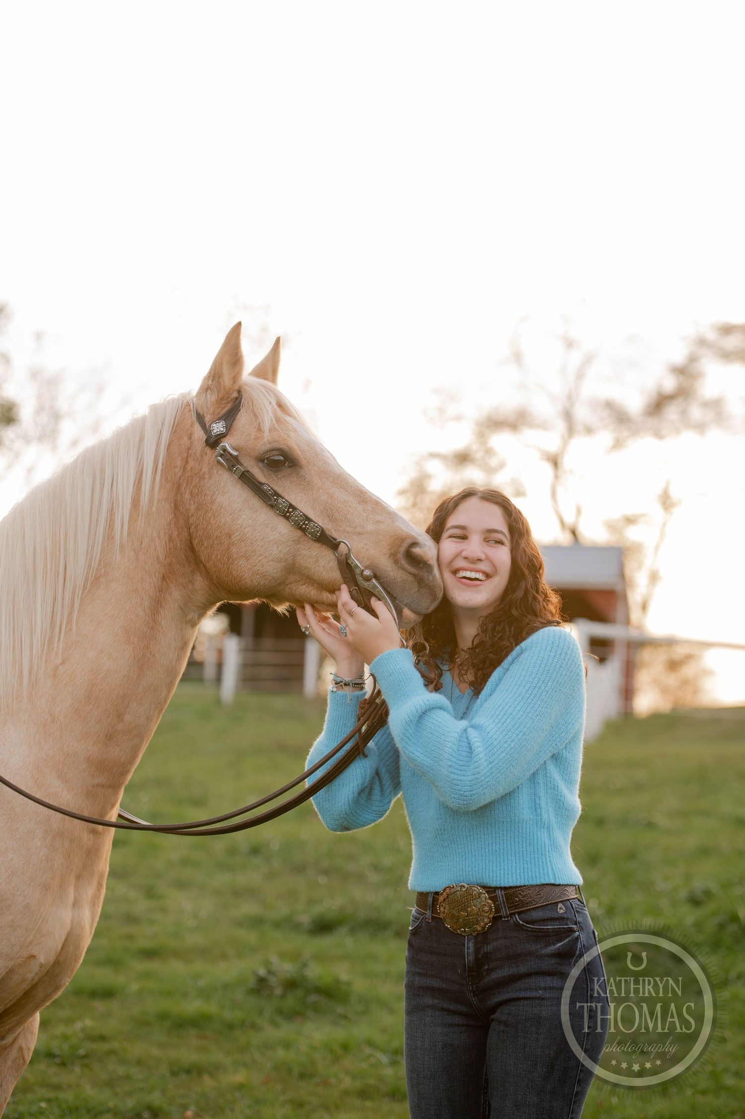 Person in blue sweater shares joyful moment with palomino horse in pasture.
