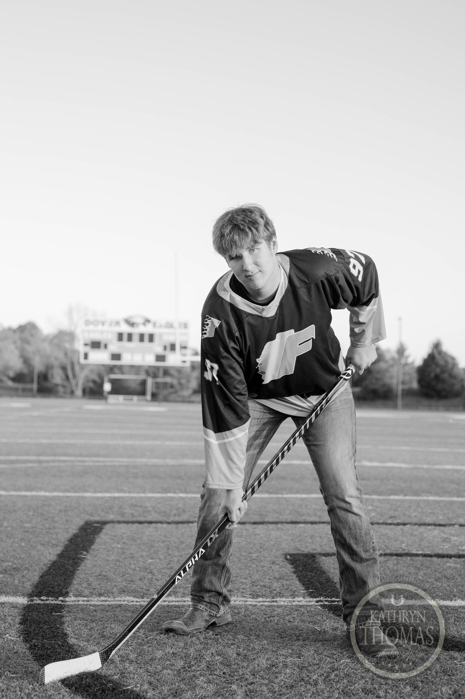 Black and white photo of hockey player posing with stick on sports field.