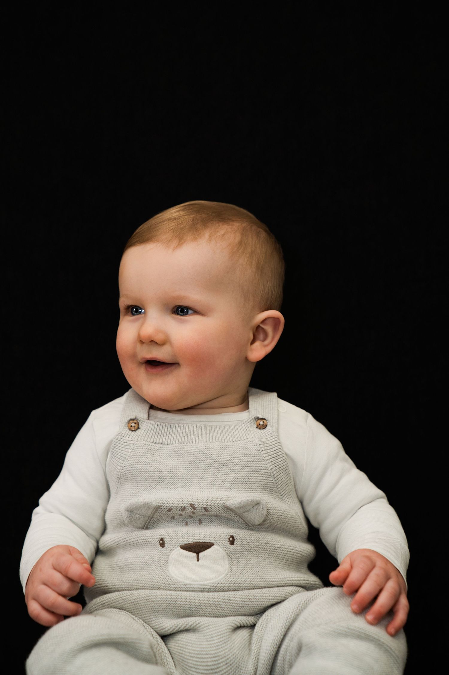 "Lachende baby in een schattig berenpakje zit voor een zwarte achtergrond. Een puur en vrolijk moment."