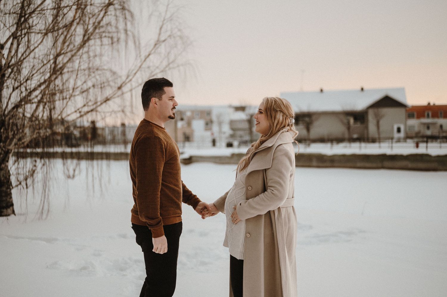 A couple holds hands in a snowy winter scene at sunset.