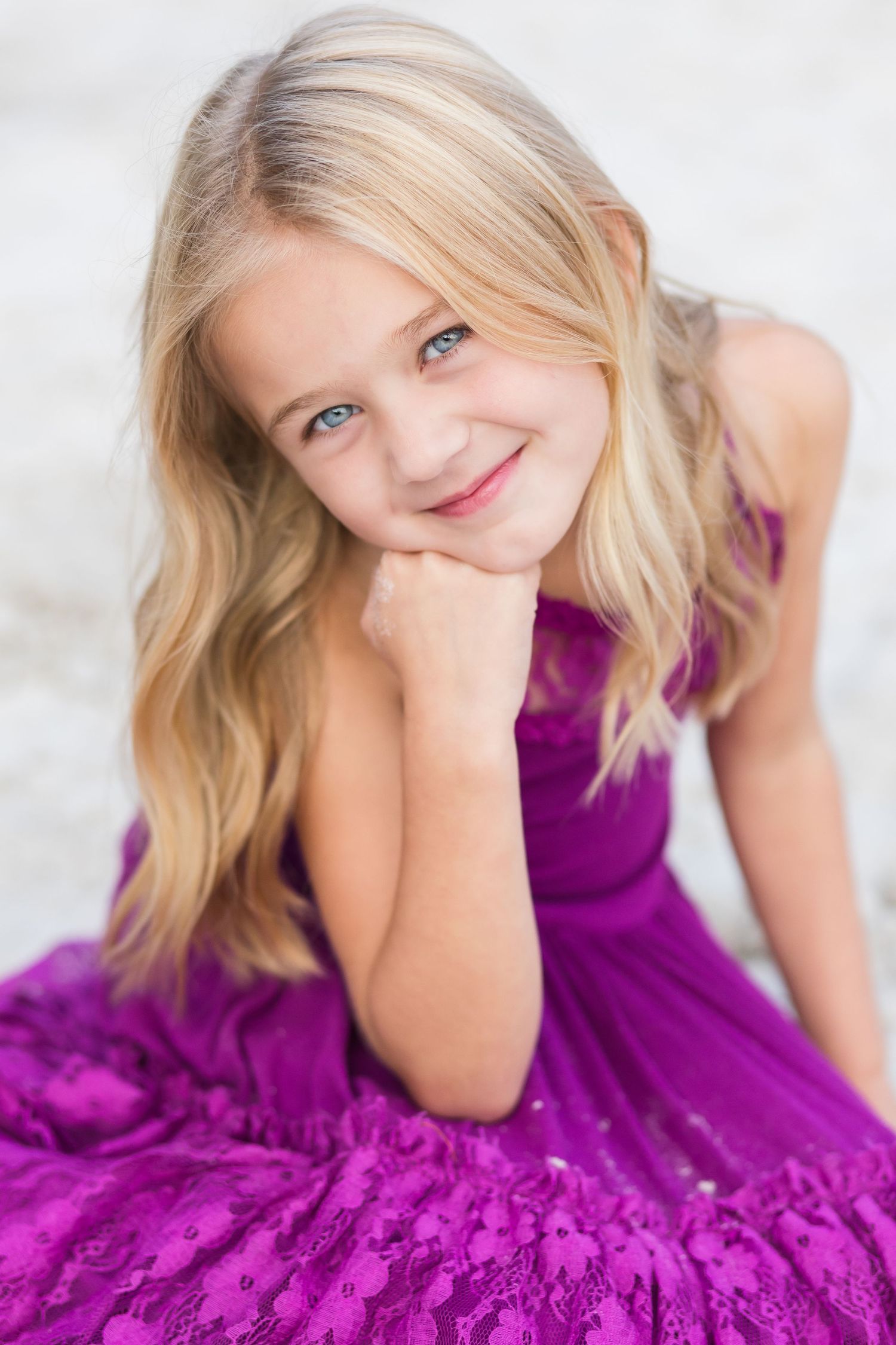 Studio portrait of someone in a vibrant purple dress with blonde hair smiling at the camera.