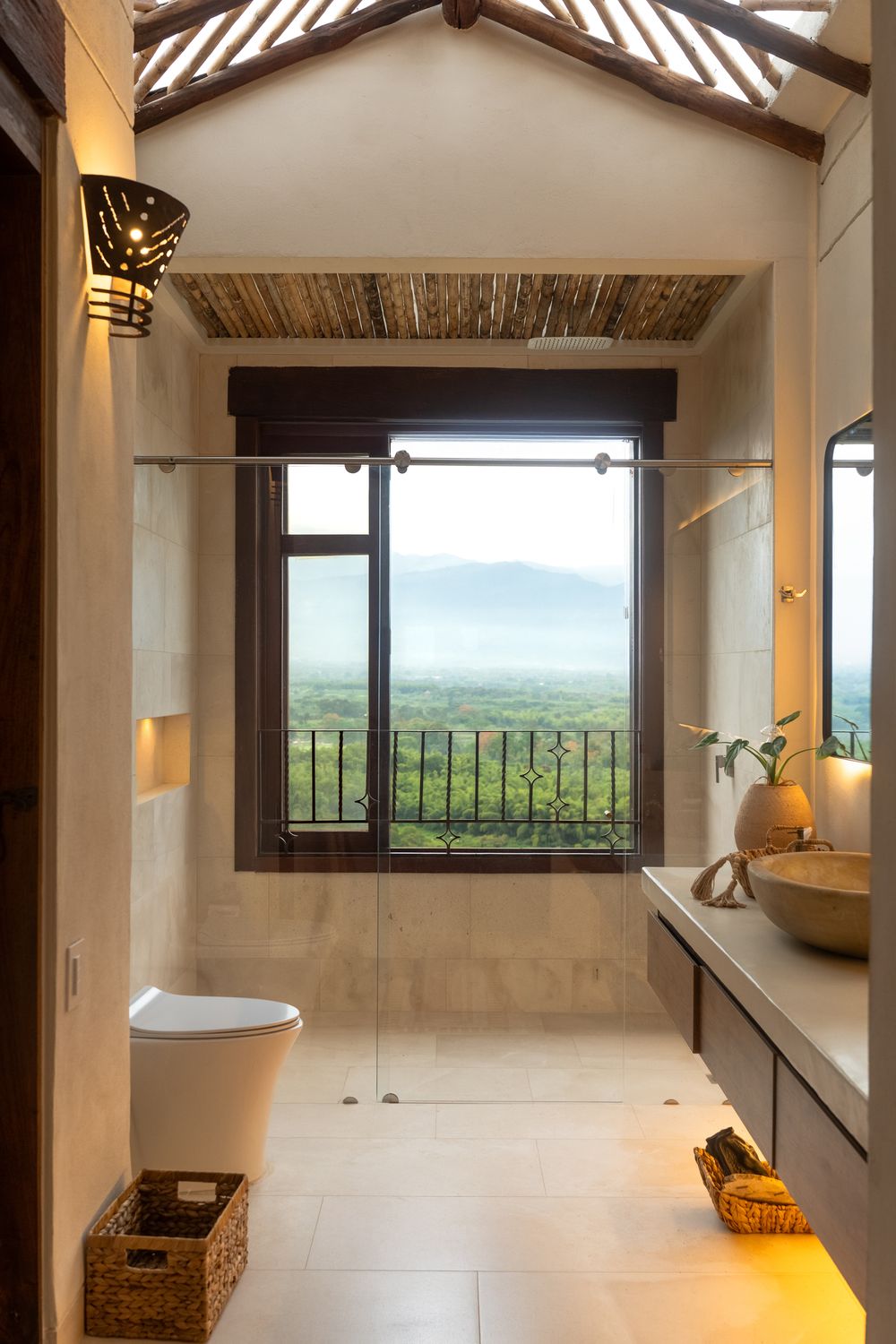 Luxury bathroom with glass shower, vessel sink, wood ceiling, and panoramic mountain view through large window.