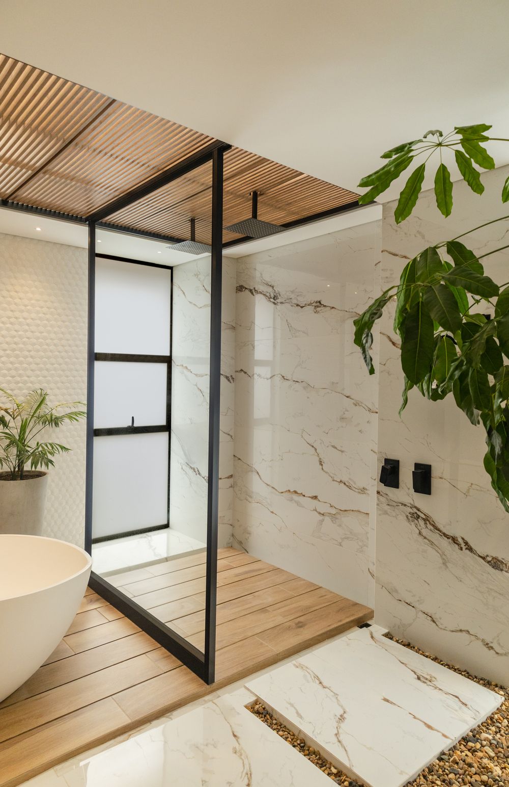 Modern luxury bathroom with marble walls, wood deck shower, black frame glass door, and tropical plants.