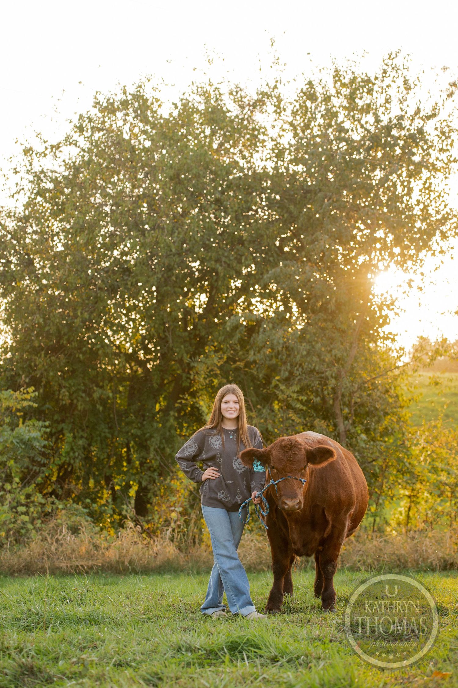 Someone stands confidently next to a large brown cow in a pastoral autumn setting.